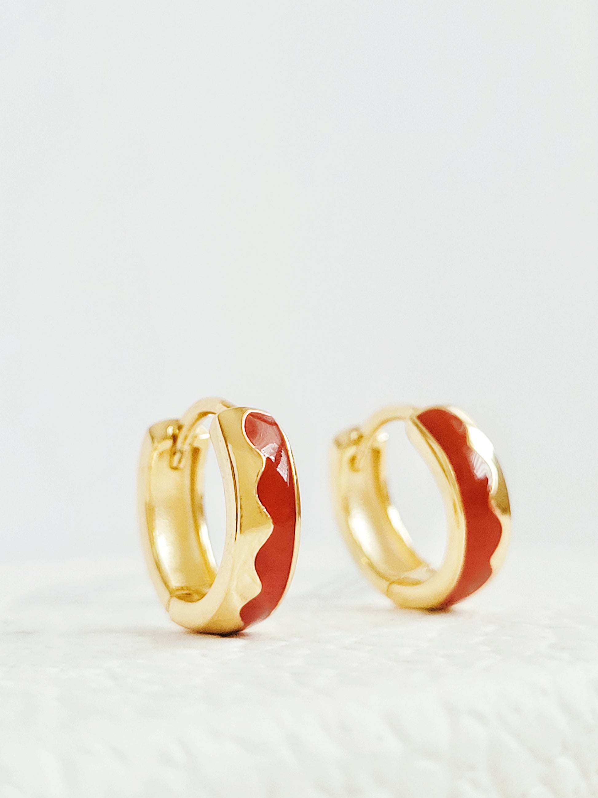 Exquisite gold-plated huggie hoop earrings adorned with vibrant red enamel, perfect for adding a touch of elegance.