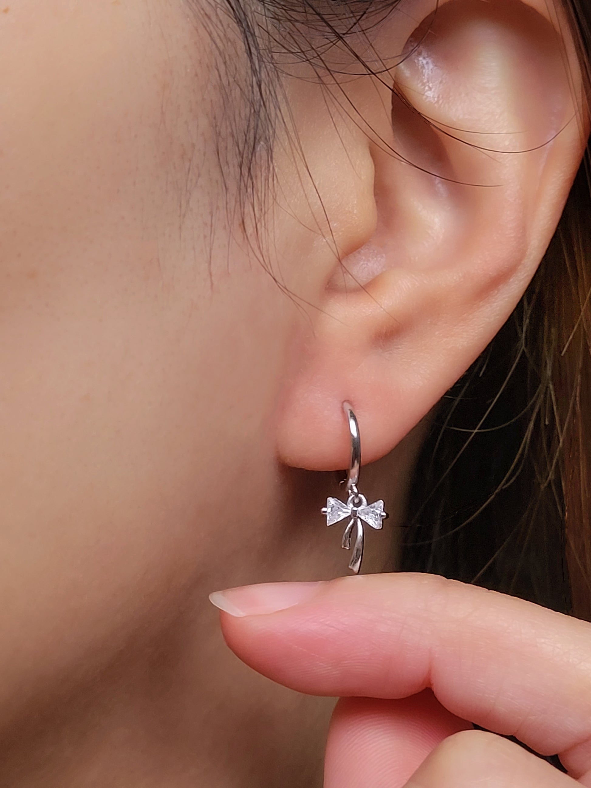 Close-up view of a woman&#39;s ear wearing silver ribbon bow earring with a dangling design, perfect for gifting to girlfriends, daughters, or loved ones.