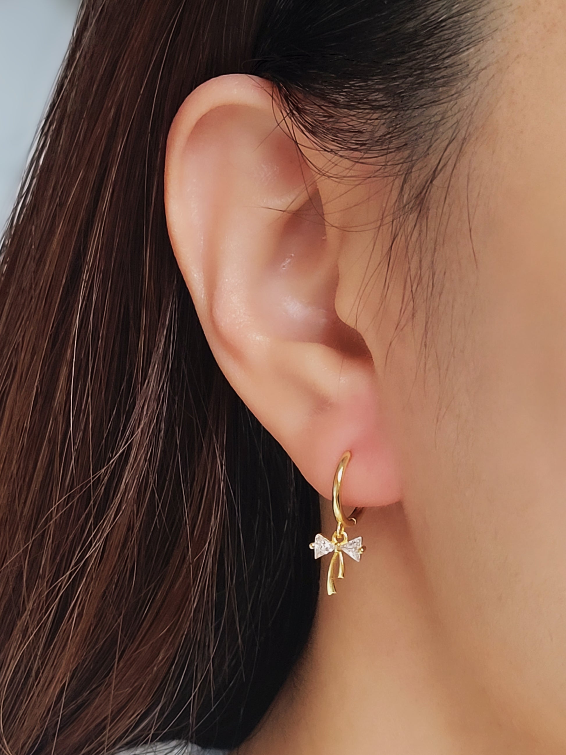 Close-up view of a woman&#39;s ear wearing gold ribbon bow earring with a dangling design, perfect for gifting to girlfriends, daughters, or loved ones.