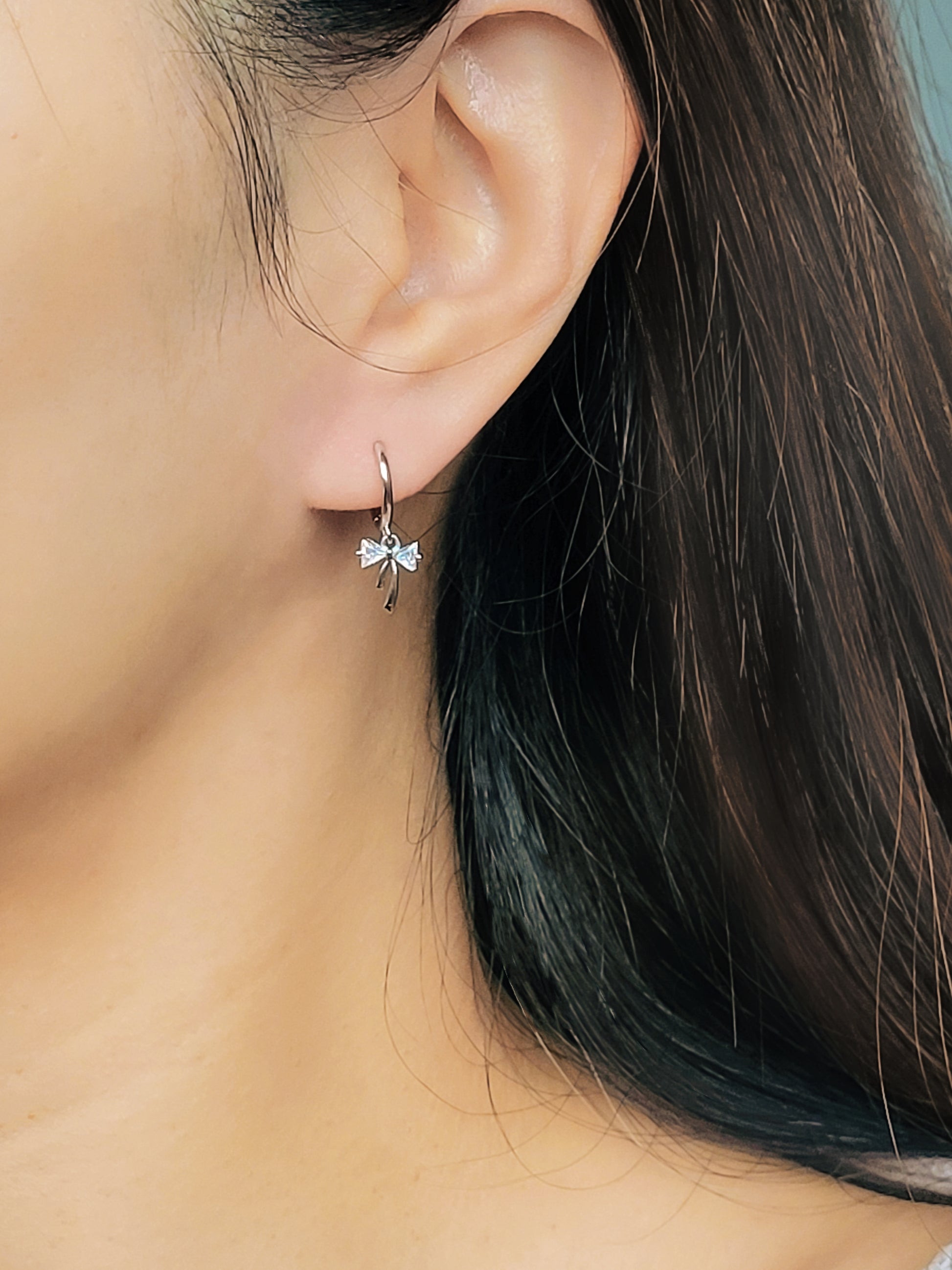 Close-up view of a woman&#39;s ear wearing silver ribbon bow earring with a dangling design, perfect for gifting to girlfriends, daughters, or loved ones.