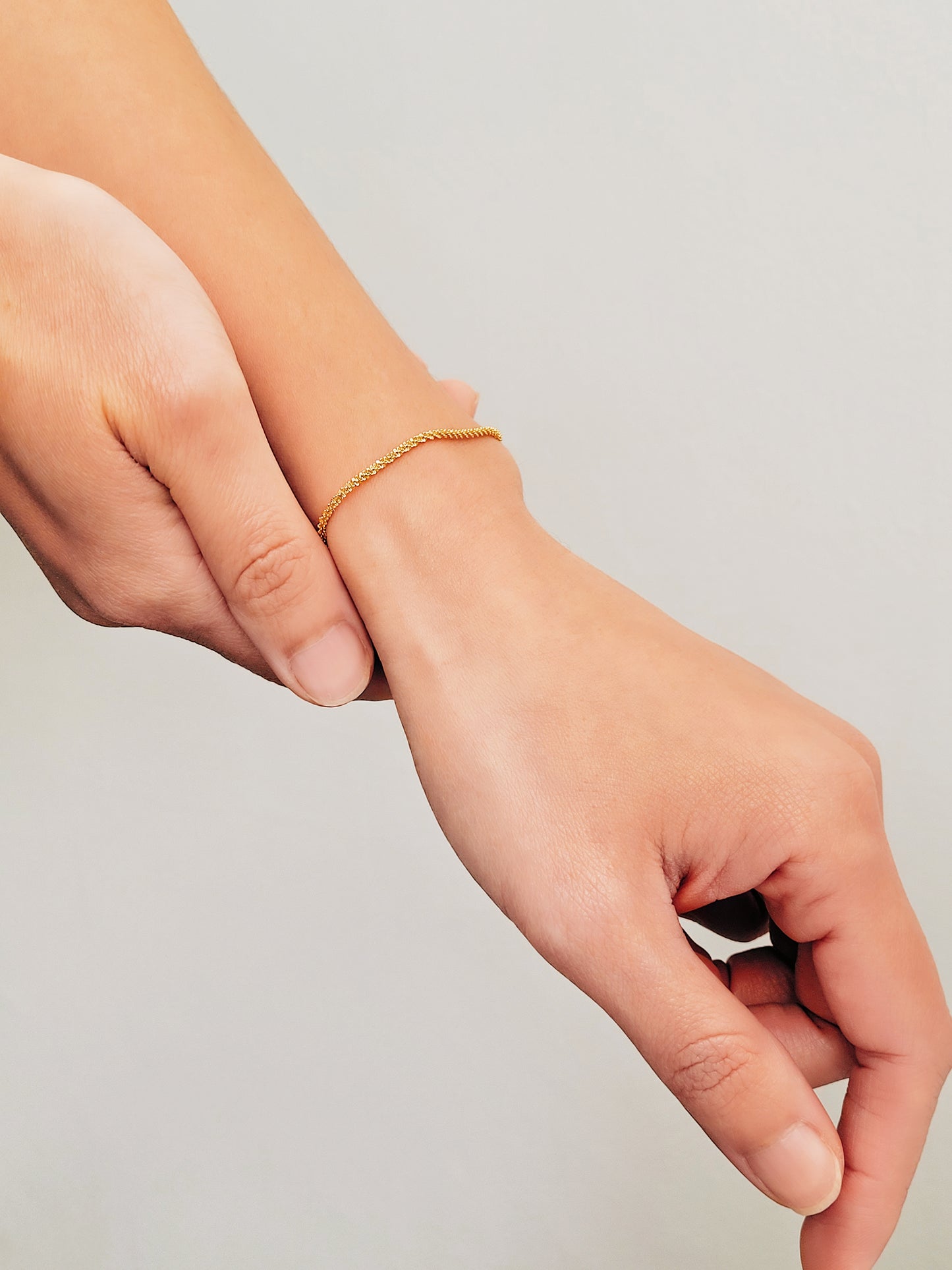 A close-up shot highlighting a woman’s wrist with a delicate gold rope bracelet.