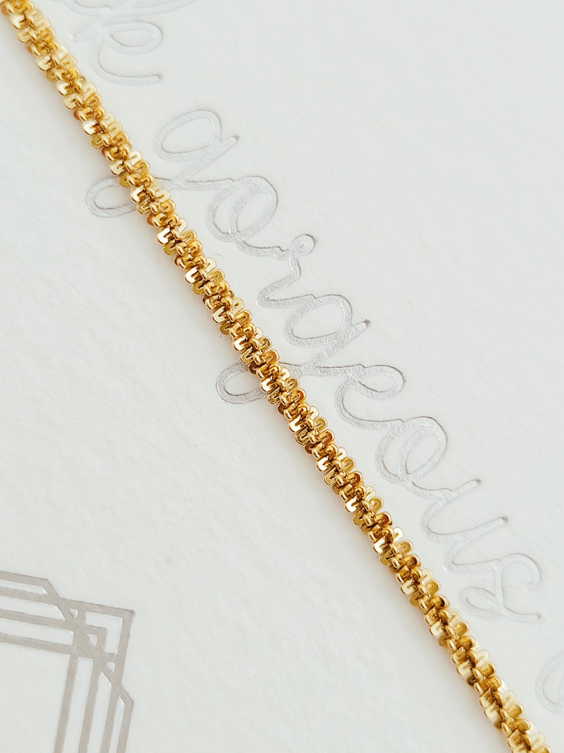 Minimalistic display of a gold rope chain bracelet with small, tightly linked rings, placed on a textured surface, emphasizing its refined detail.