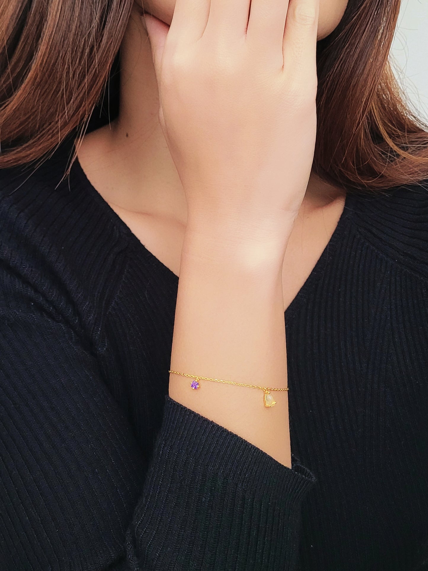 A woman wears a refined gold bracelet, highlighted by a striking Gold Rutilated Quartz and a charming Lilac Amethyst charms.