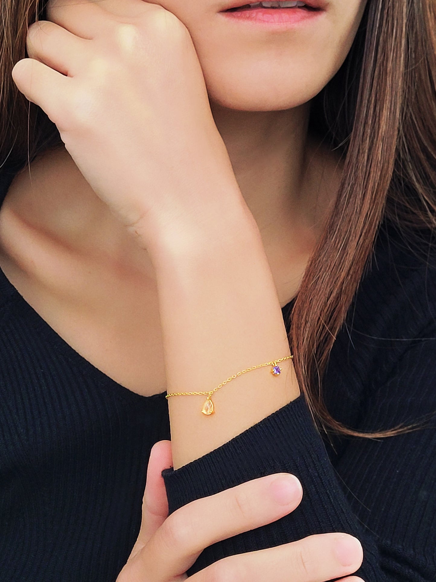 A woman elegantly showcases a gold bracelet adorned with a stunning Gold  Rutilated Quartz and Amethyst charms.