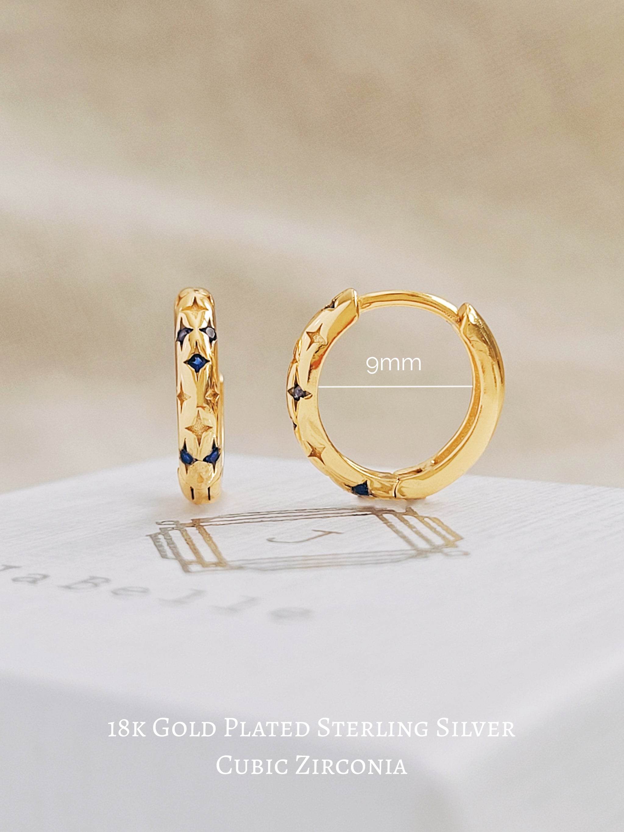 close up of a pair of blue huggie earrings with detailed stars, displayed on a jewellery box