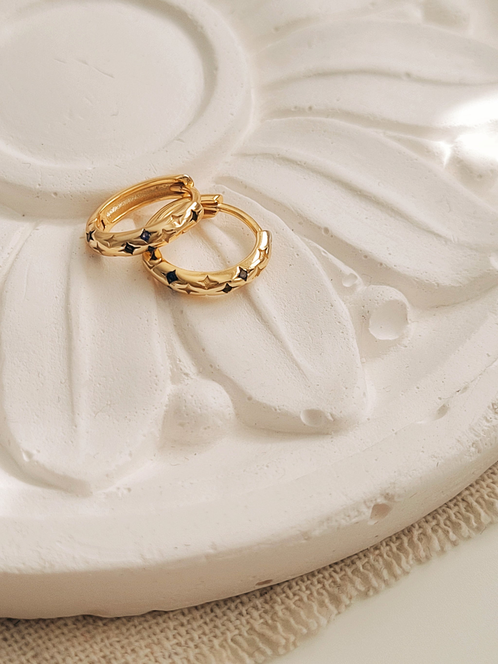 A pair of blue star huggie earrings displayed on a white flower surface. 