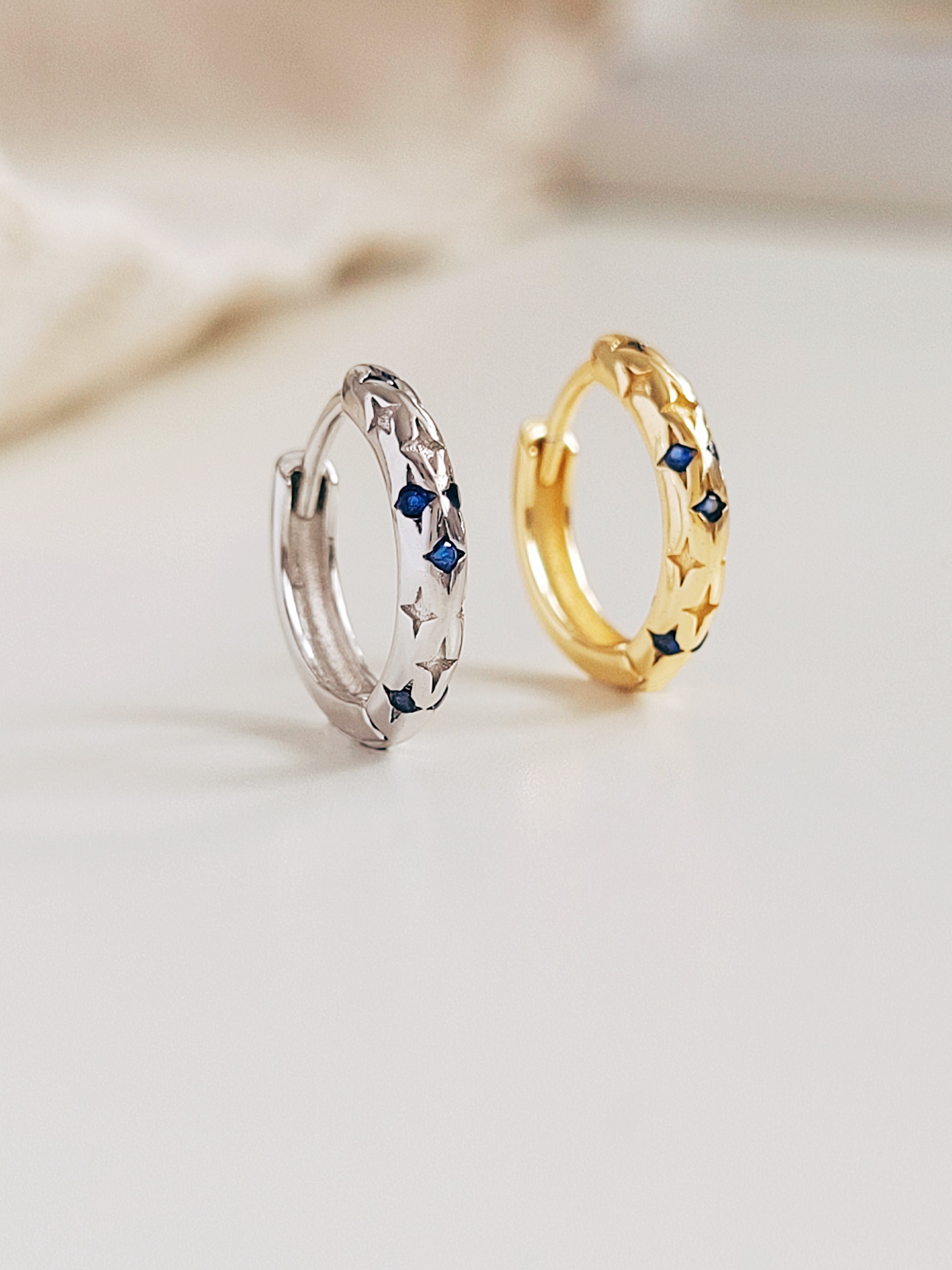 Two hoop earrings, one gold and one silver, with embedded blue stones on a light background.