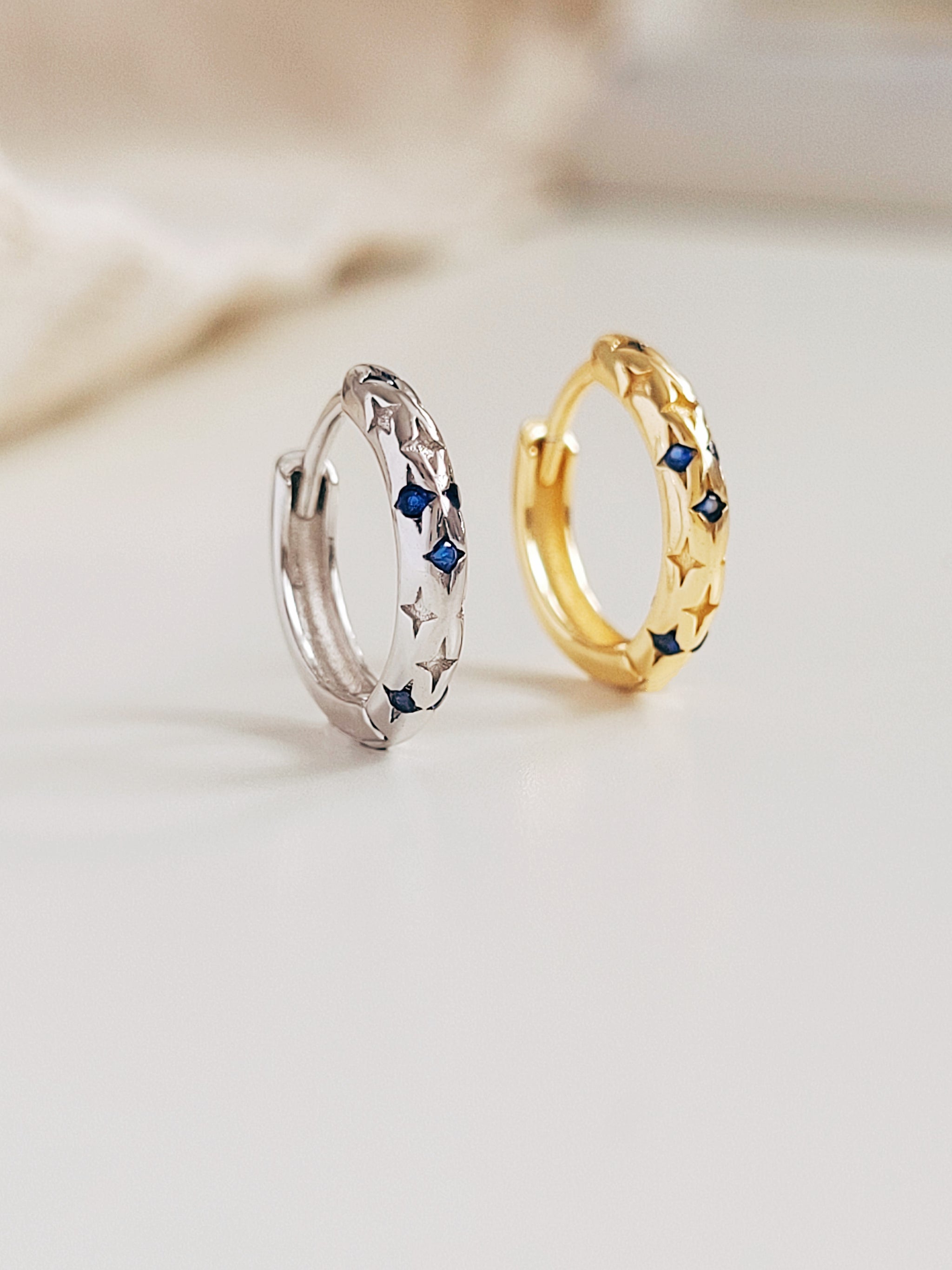 Two hoop earrings, one gold and one silver, with embedded blue stones on a light background.