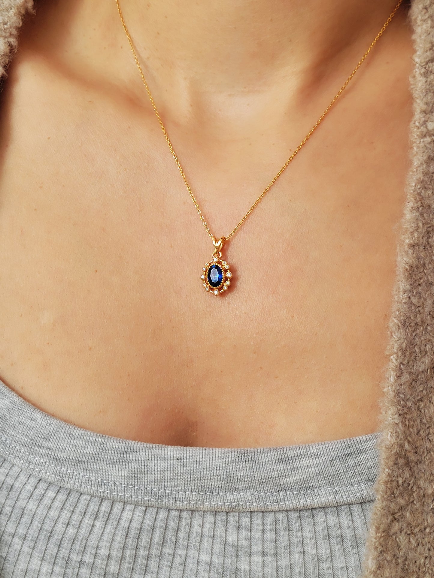 This image features a close-up view of a woman wearing a delicate and elegant Sapphire CZ diamond necklace. The necklace has a gold chain that provides a classic and sophisticated touch.