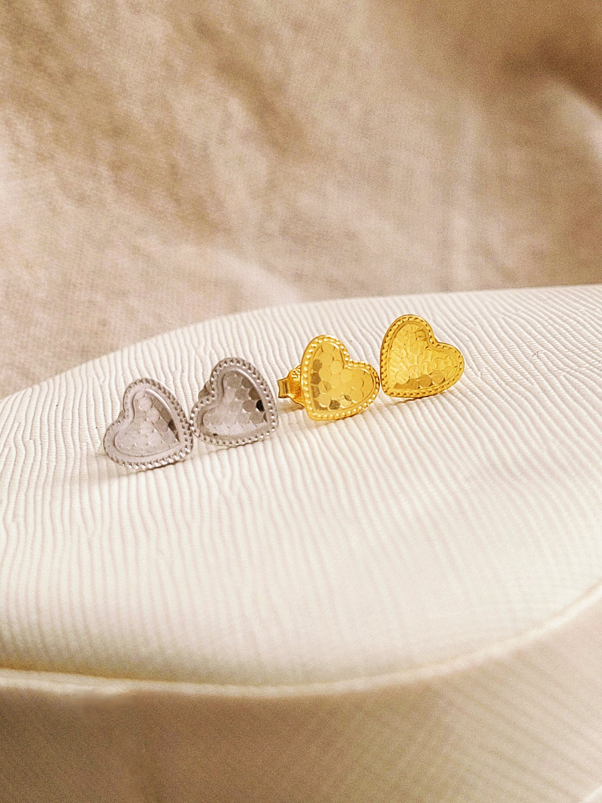 Textured heart earrings in gold and silver on a beige surface