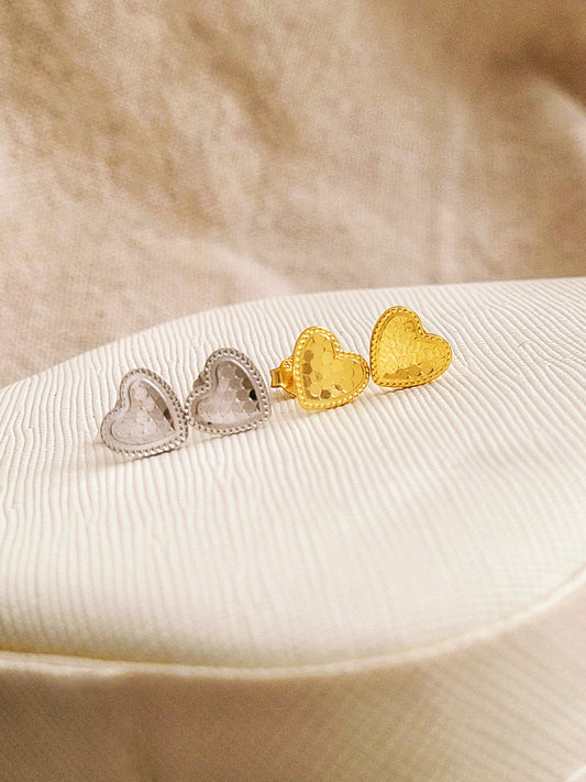 Textured heart earrings in gold and silver on a beige surface