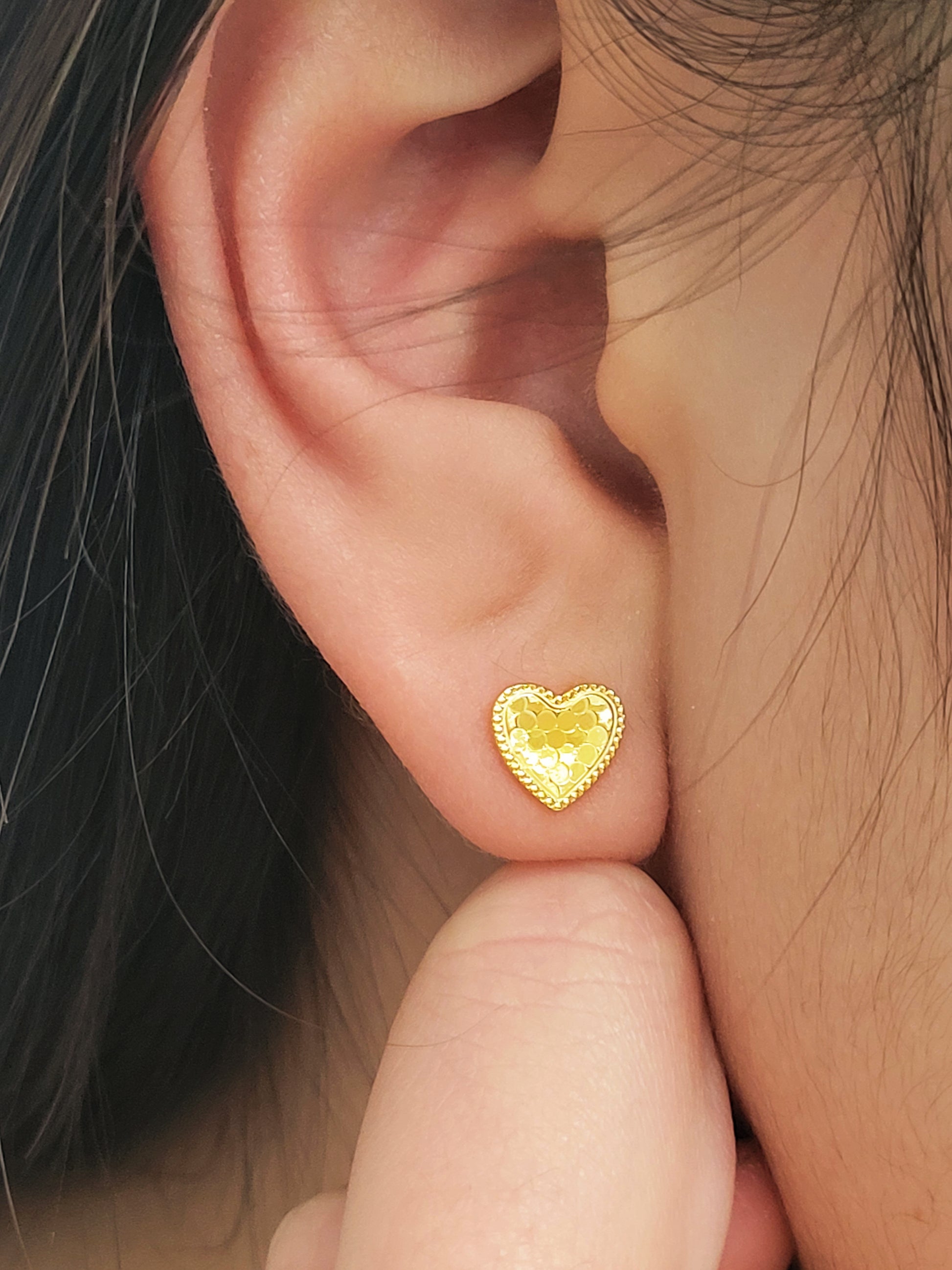 Close up of a woman wearing 18k gold plated heart stud earrings with sparkling texture