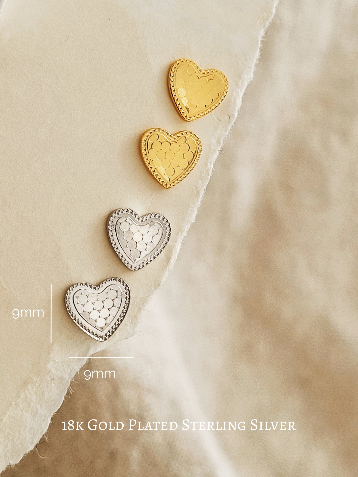 Pairs of gold heart studs and silver heart studs displayed on a beige paper with dimensions.