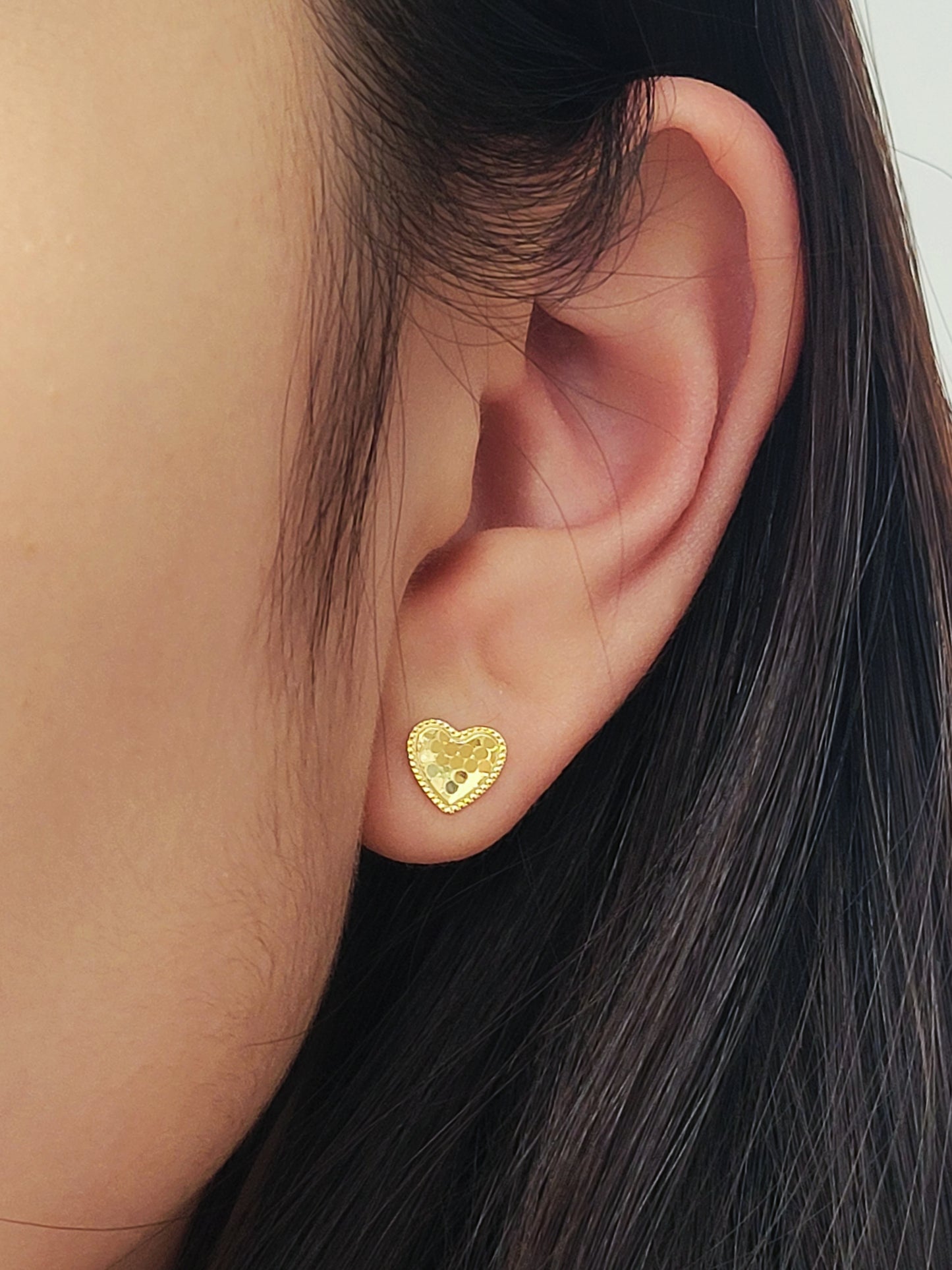Close-up of an ear wearing a minimalist elegant gold heart stud earring.