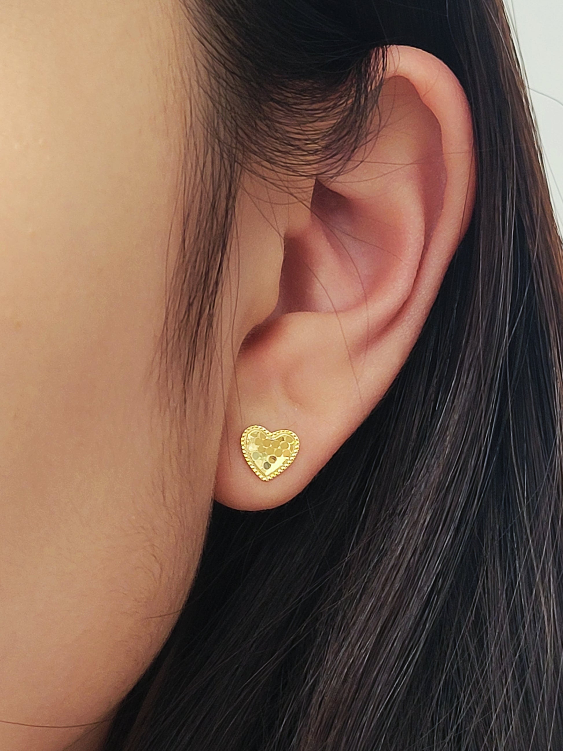 Close-up of an ear wearing a minimalist elegant gold heart stud earring.
