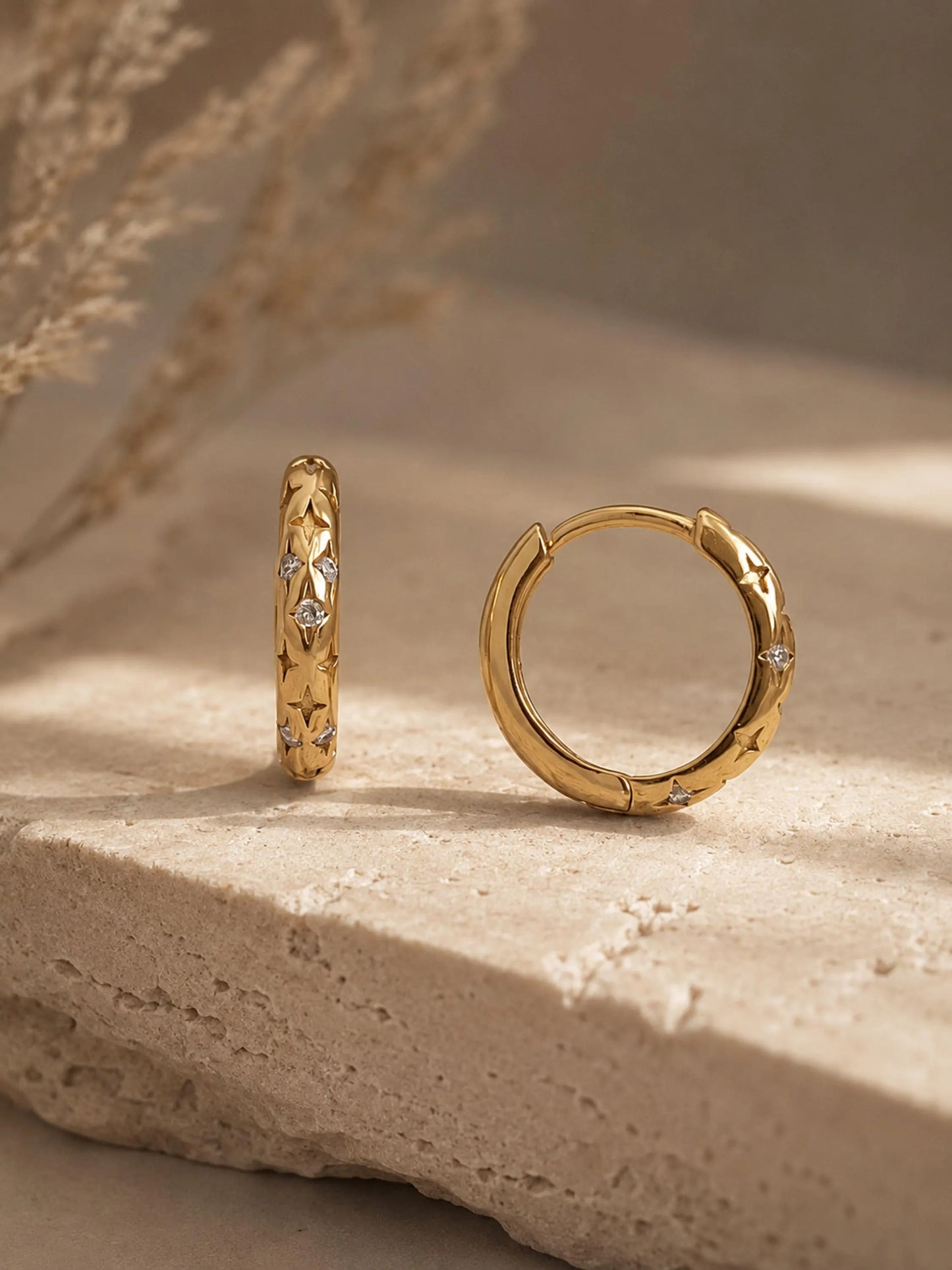 Pair of 18k gold plated sterling silver star huggie hoop earrings with cubic zirconia stones displayed on a textured stone surface.