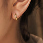 Close-up of a woman wearing a gold star huggie hoop earring on her ear lobe.
