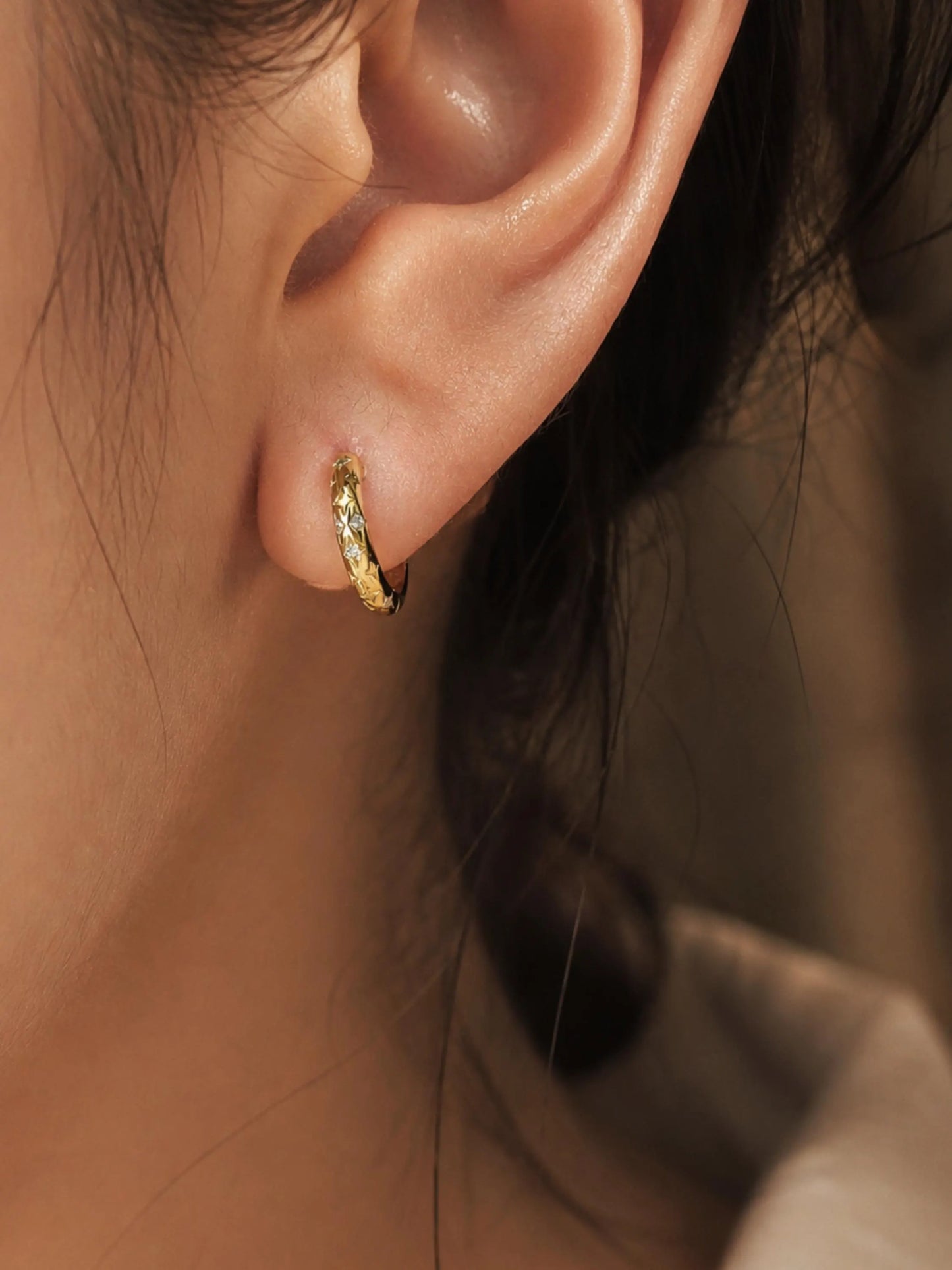 Close-up of a woman wearing a gold star huggie hoop earring on her ear lobe.