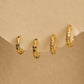 Set of small gold hoop earrings with embedded stones with star pattern on a beige background