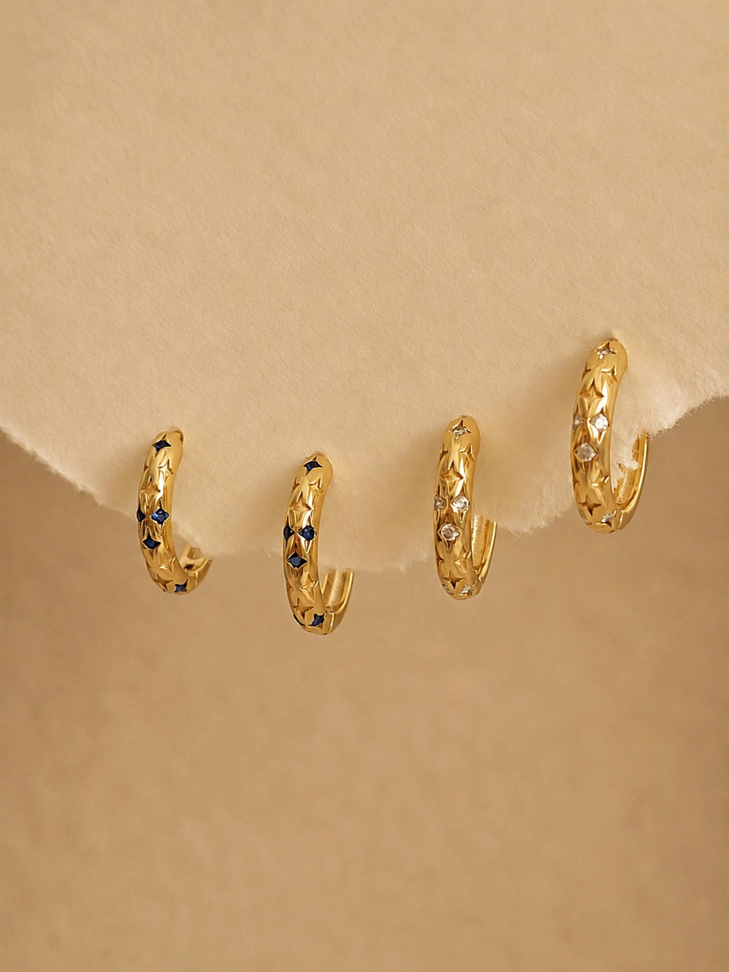 Set of small gold hoop earrings with embedded stones with star pattern on a beige background
