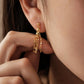 A close-up of a model's ear wearing a delicate gold tassel chain earring with dangling chain and bead fringe crafted in 18k gold plated sterling silver.
