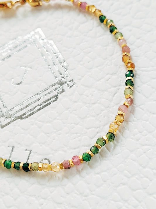A multicolored tourmaline beaded bracelet with gold nuggets, displayed on a white surface.
