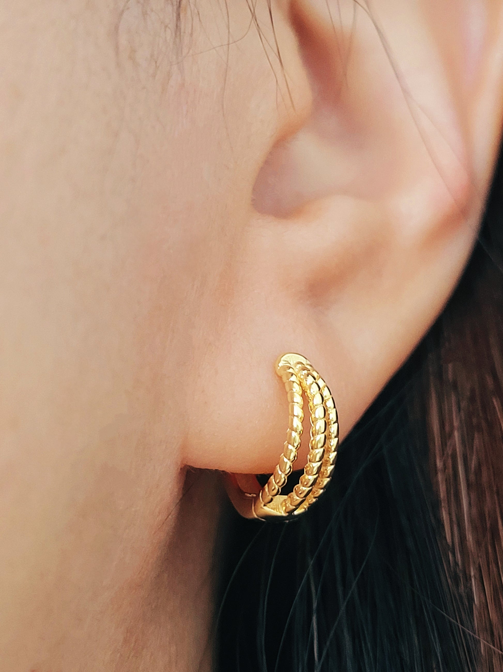 Close up of a woman wearing a minimalist triple hoop twisted huggie earrings crafted in 18k gold plated sterling silver.