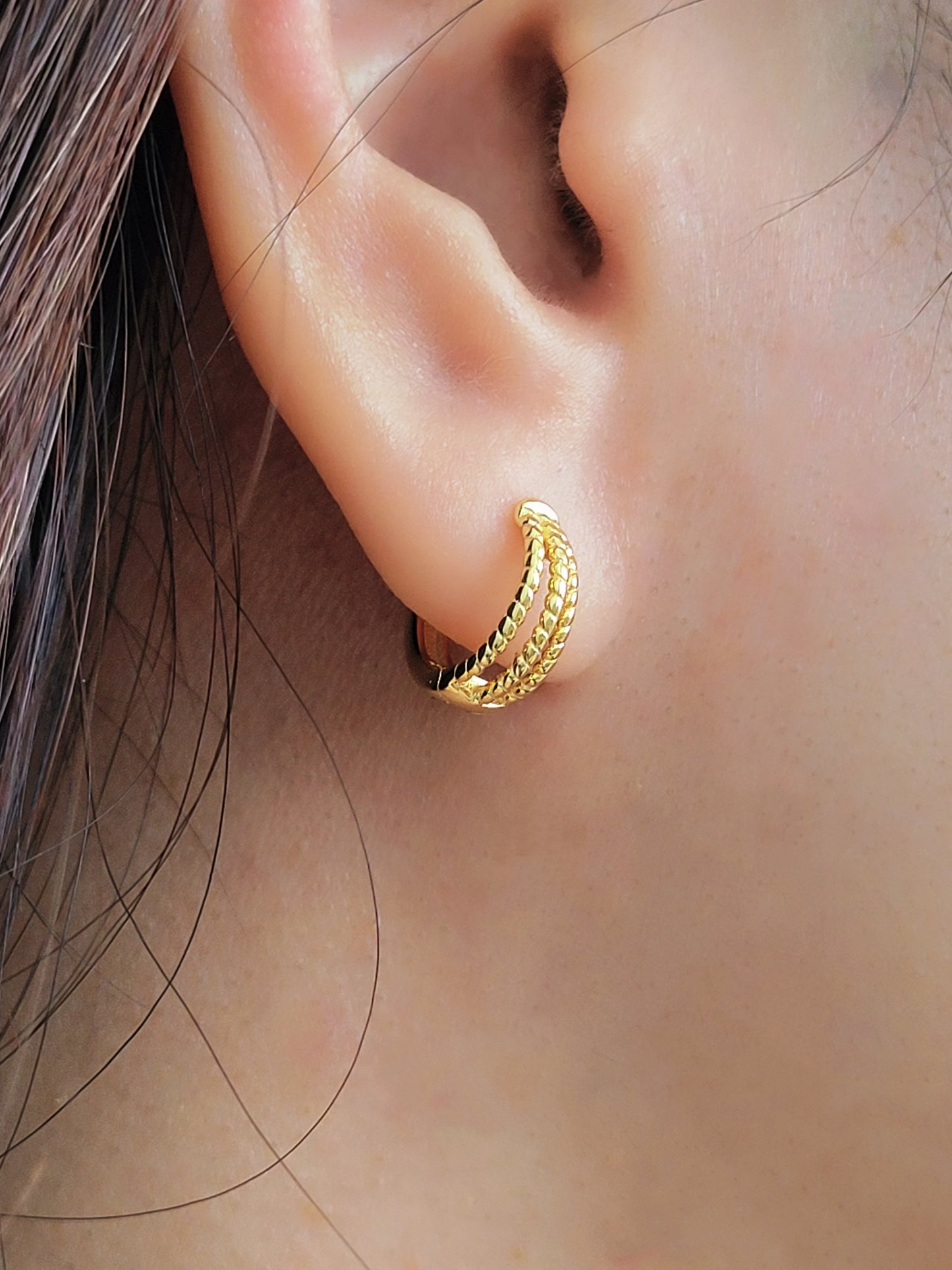 Close up of a woman wearing a minimalist triple hoop twisted huggie earrings crafted in 18k gold plated sterling silver.