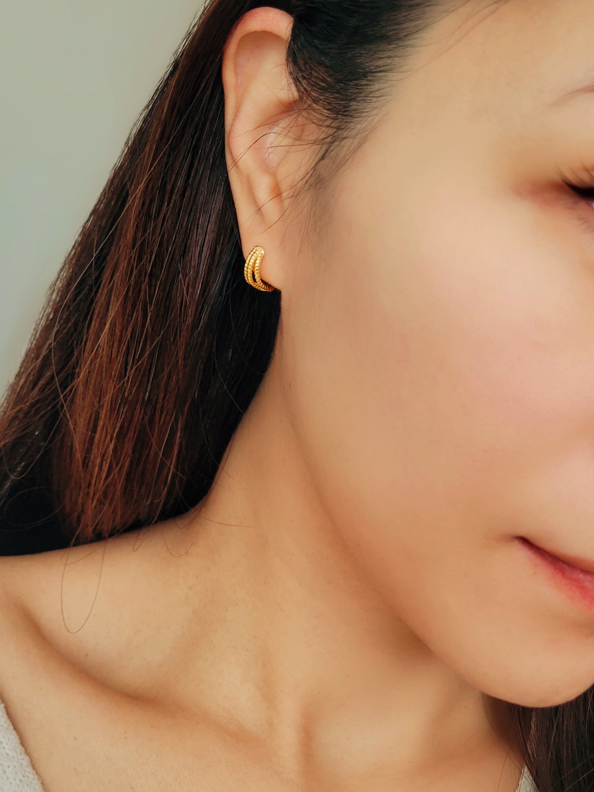 Close up of a woman wearing a minimalist triple hoop twisted huggie earrings crafted in 18k gold plated sterling silver.