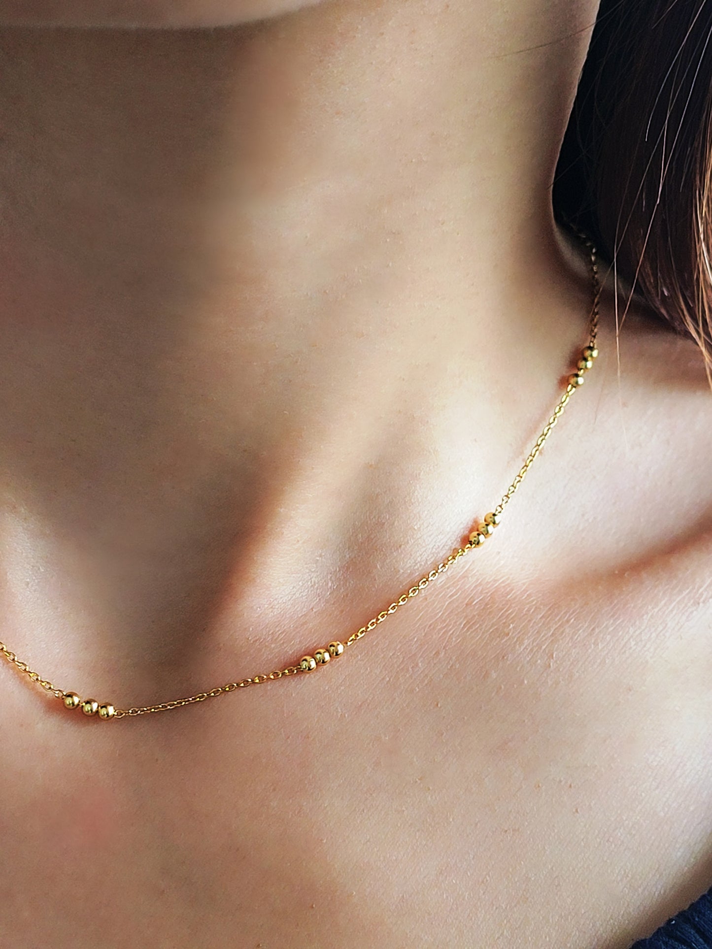 Close-up of a woman wearing a delicate 18ct gold vermeil triple ball necklace, showcasing its minimalist design with small gold beads spaced along a fine chain.