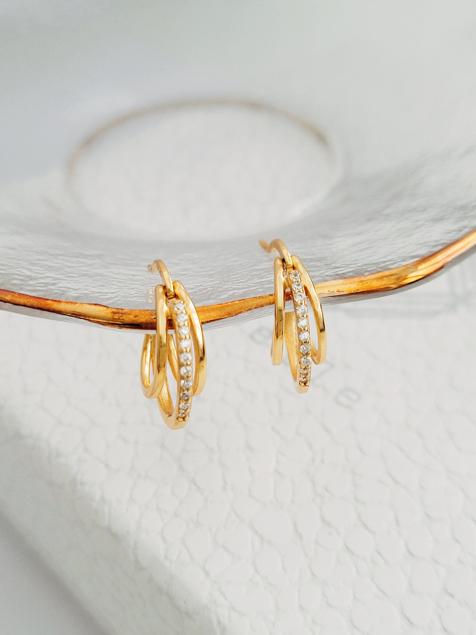 Triple gold hoop earrings, each hoop interlocking with a bold and gleaming finish, accented with sparkling stones, making a striking, luxurious statement