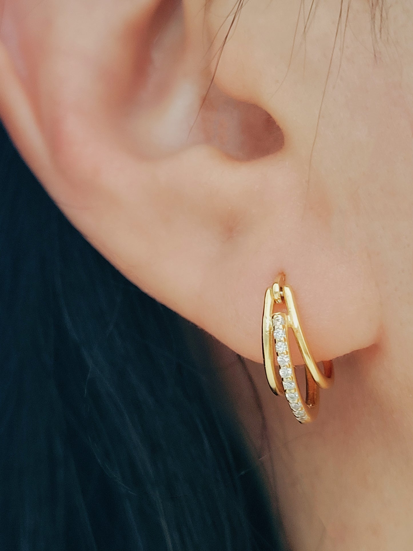 A woman elegantly adorned with triple gold hoop earrings, each hoop shimmering with a refined, polished finish, exuding a sense of sophistication and timeless luxury.