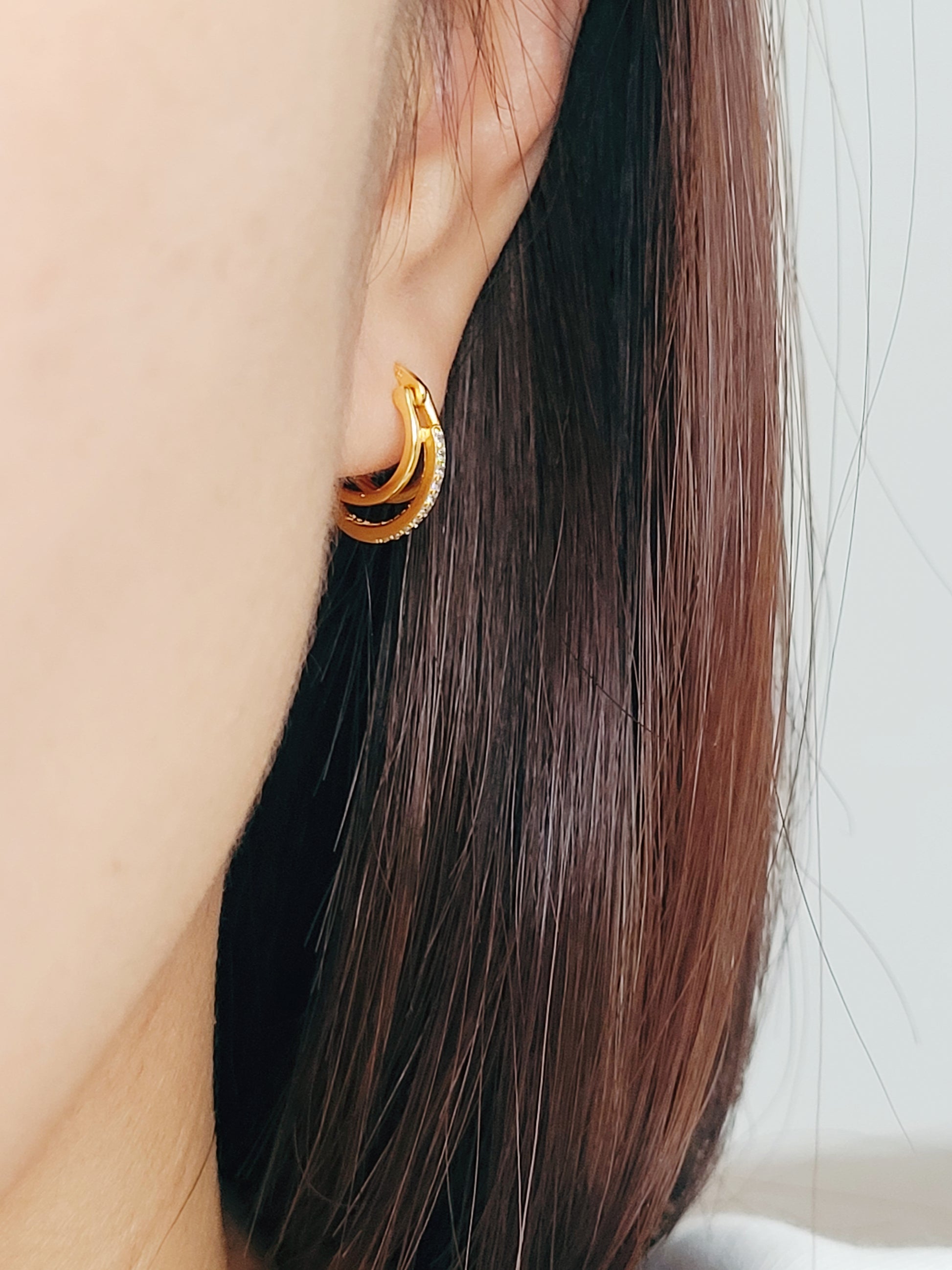 A woman gracefully wearing triple gold hoop earrings, each hoop radiating a subtle, polished brilliance, embodying elegance and high-end sophistication