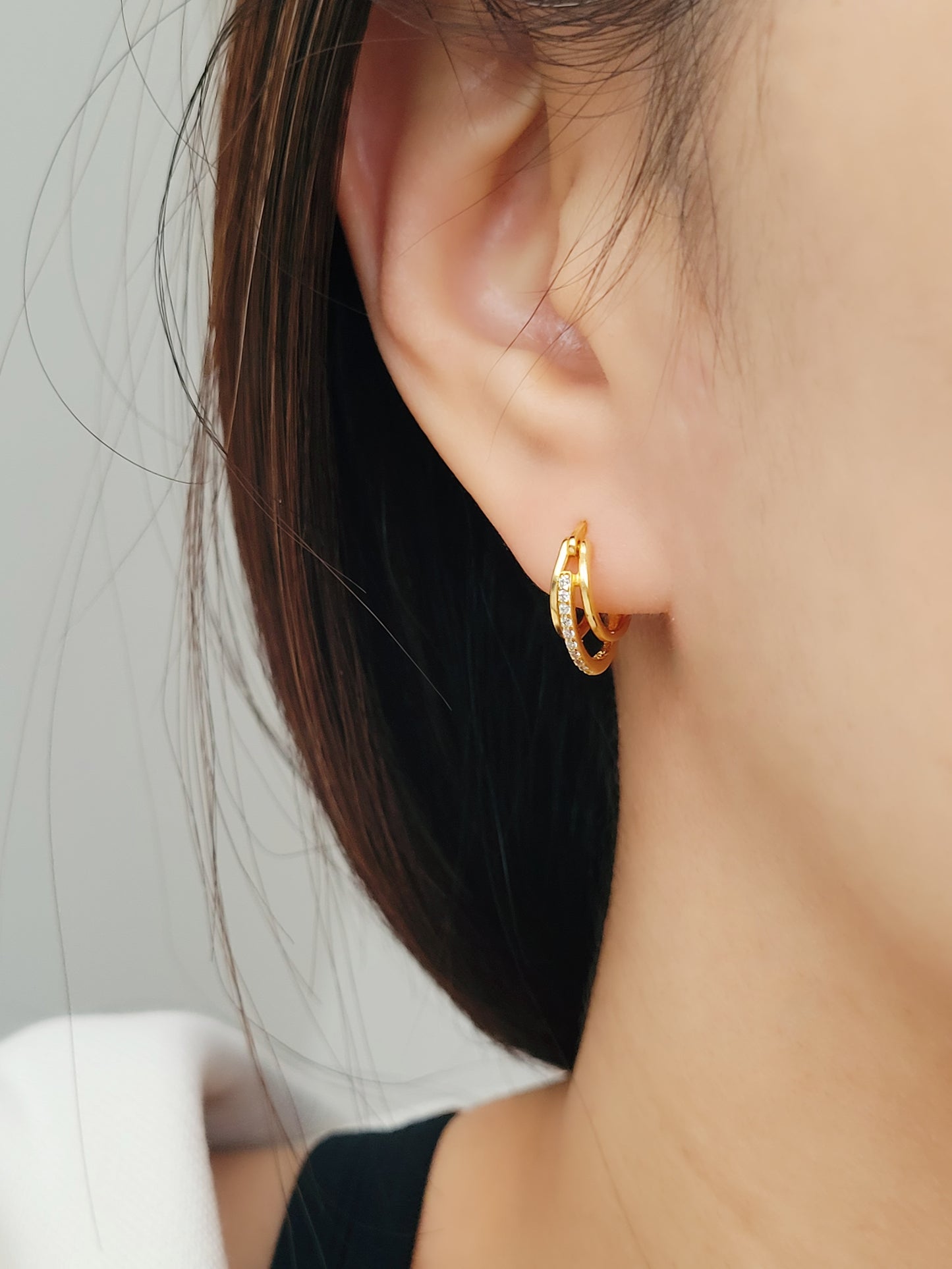 A woman flaunting triple gold hoop earrings, each hoop catching the light with an edgy, striking brilliance that commands attention.