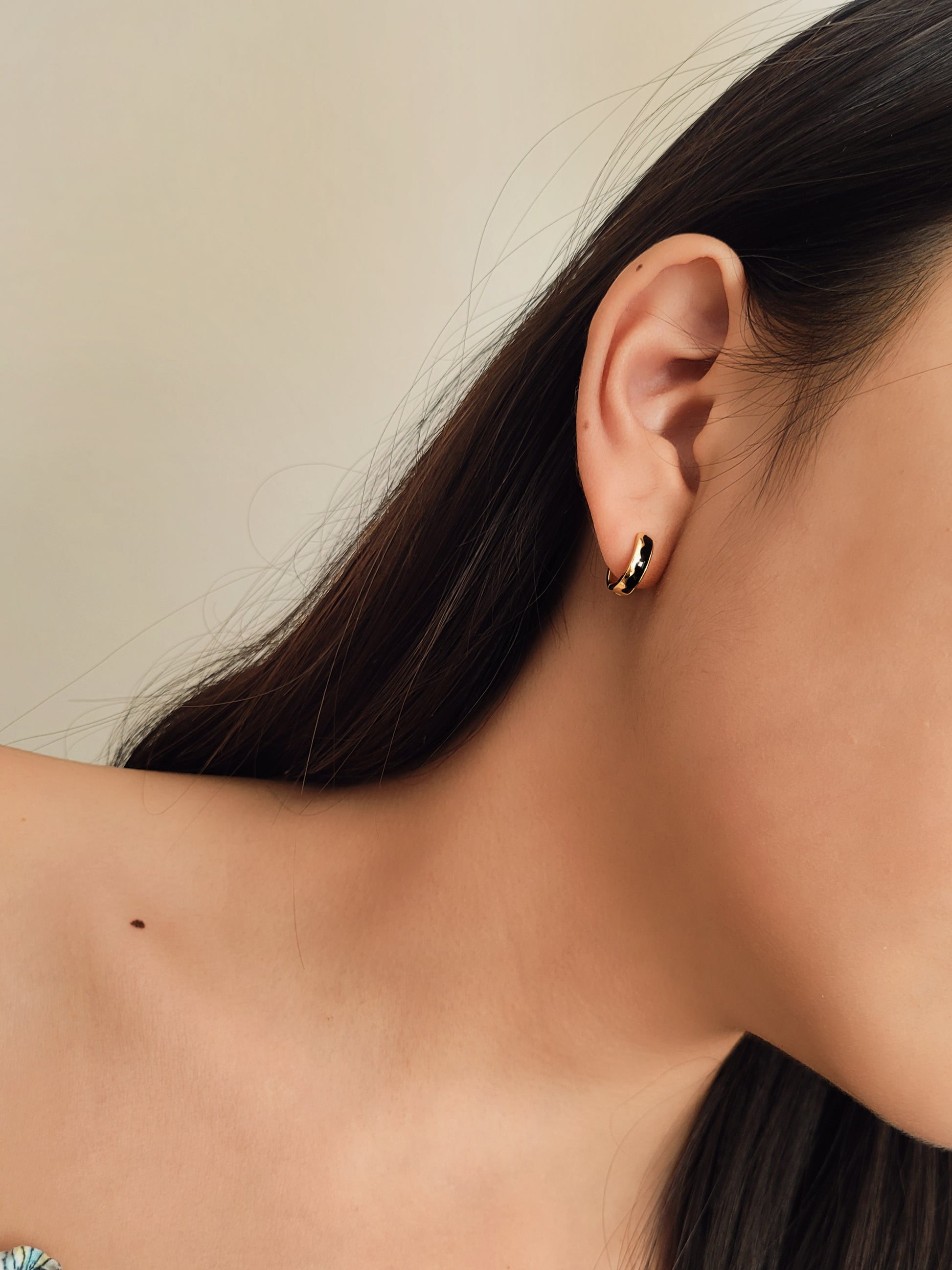 Close-up of a woman wearing a gold huggie earring with black enamel wavy pattern