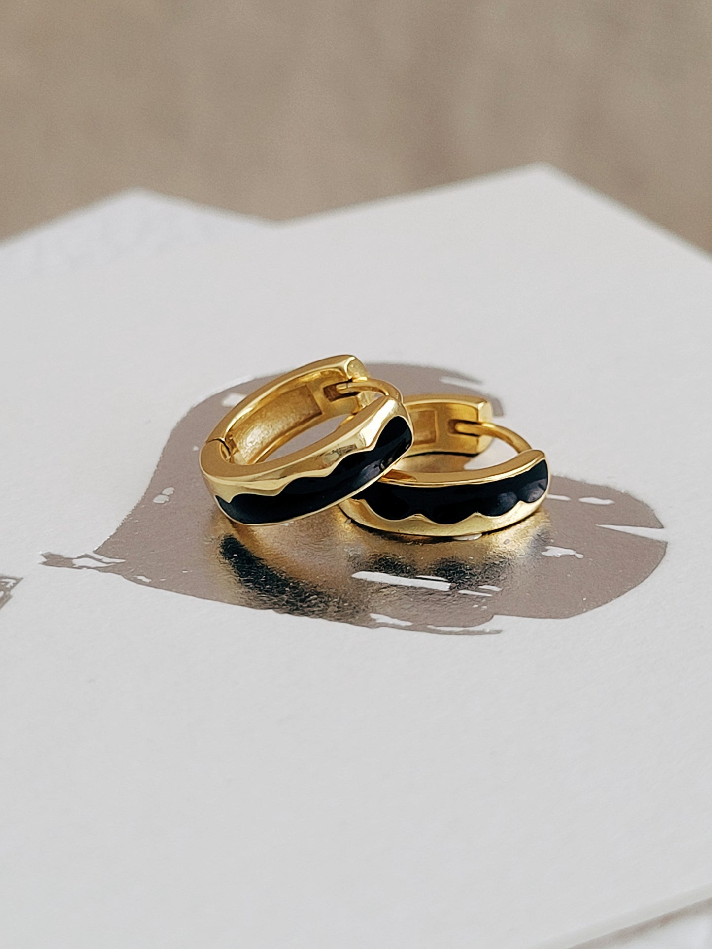 Gold hoop earrings with black enamel on a white surface