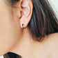 Close-up of an ear wearing a small hoop earring with black enamel 
