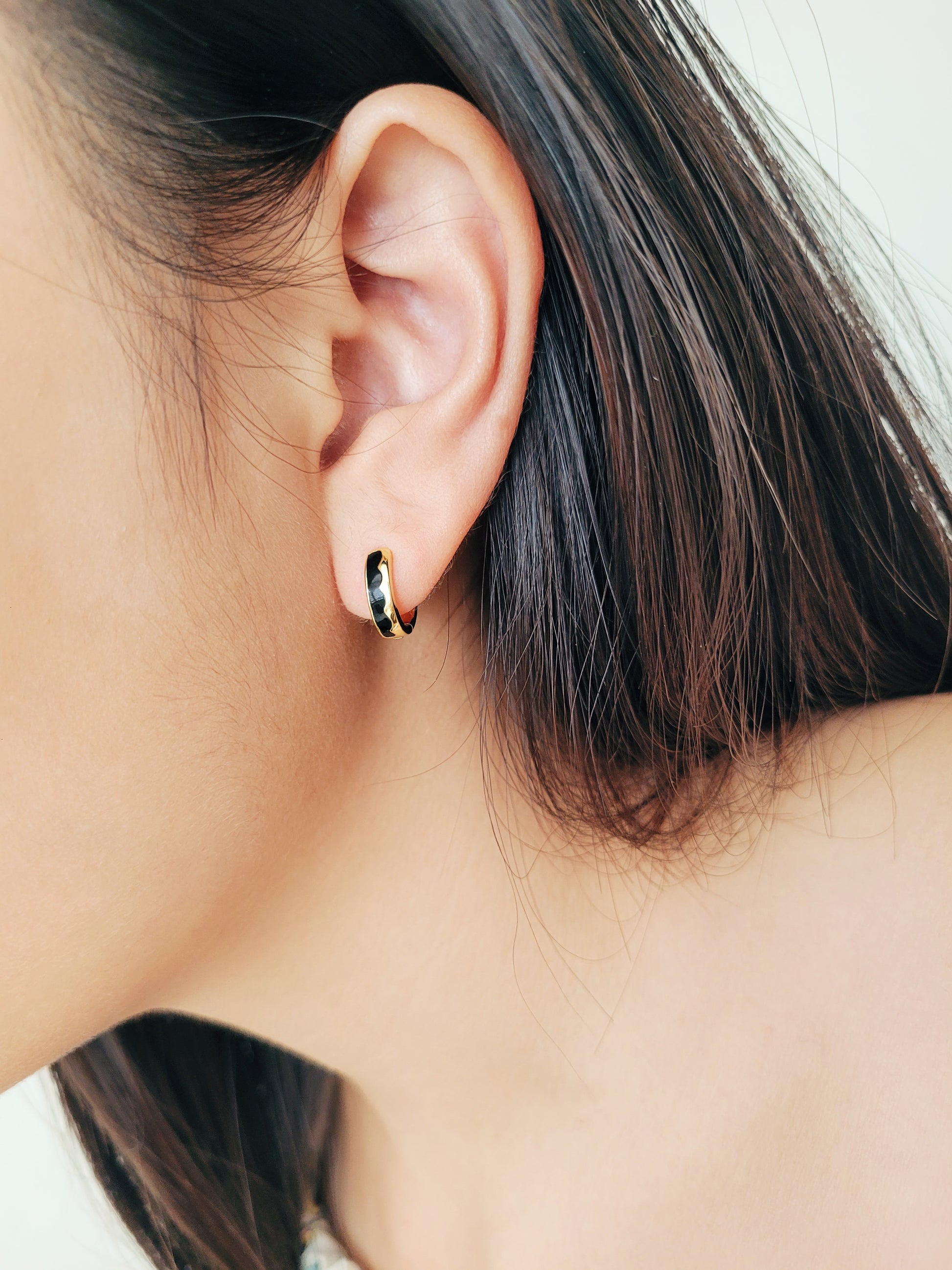 Close-up of an ear wearing a small hoop earring with black enamel 