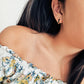 Close-up of a person wearing a floral off-shoulder top with an edgy black enamel huggie earring.
