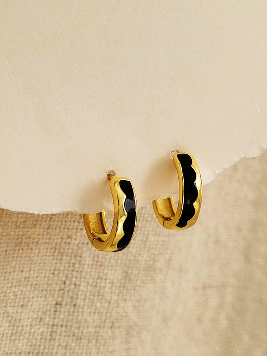 Gold hoop earrings with wavy black enamel on a textured beige surface
