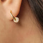 Side view of a woman wearing dainty small gold hoop earrings with white enamel bead
