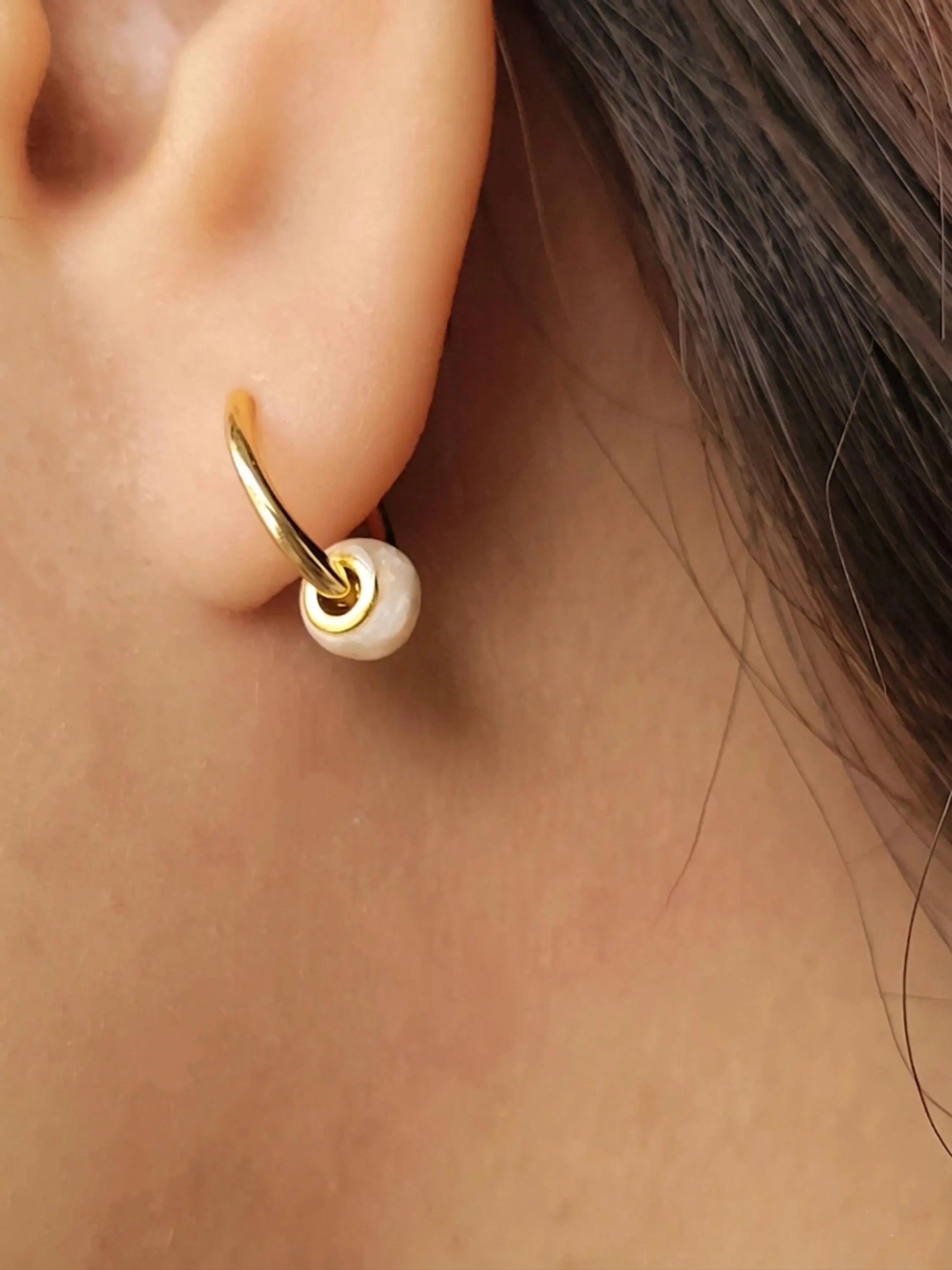 Side view of a woman wearing dainty small gold hoop earrings with white enamel bead