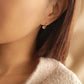 A woman wearing a gold hoop earring with a small white bead charm, minimalist and dainty style.
