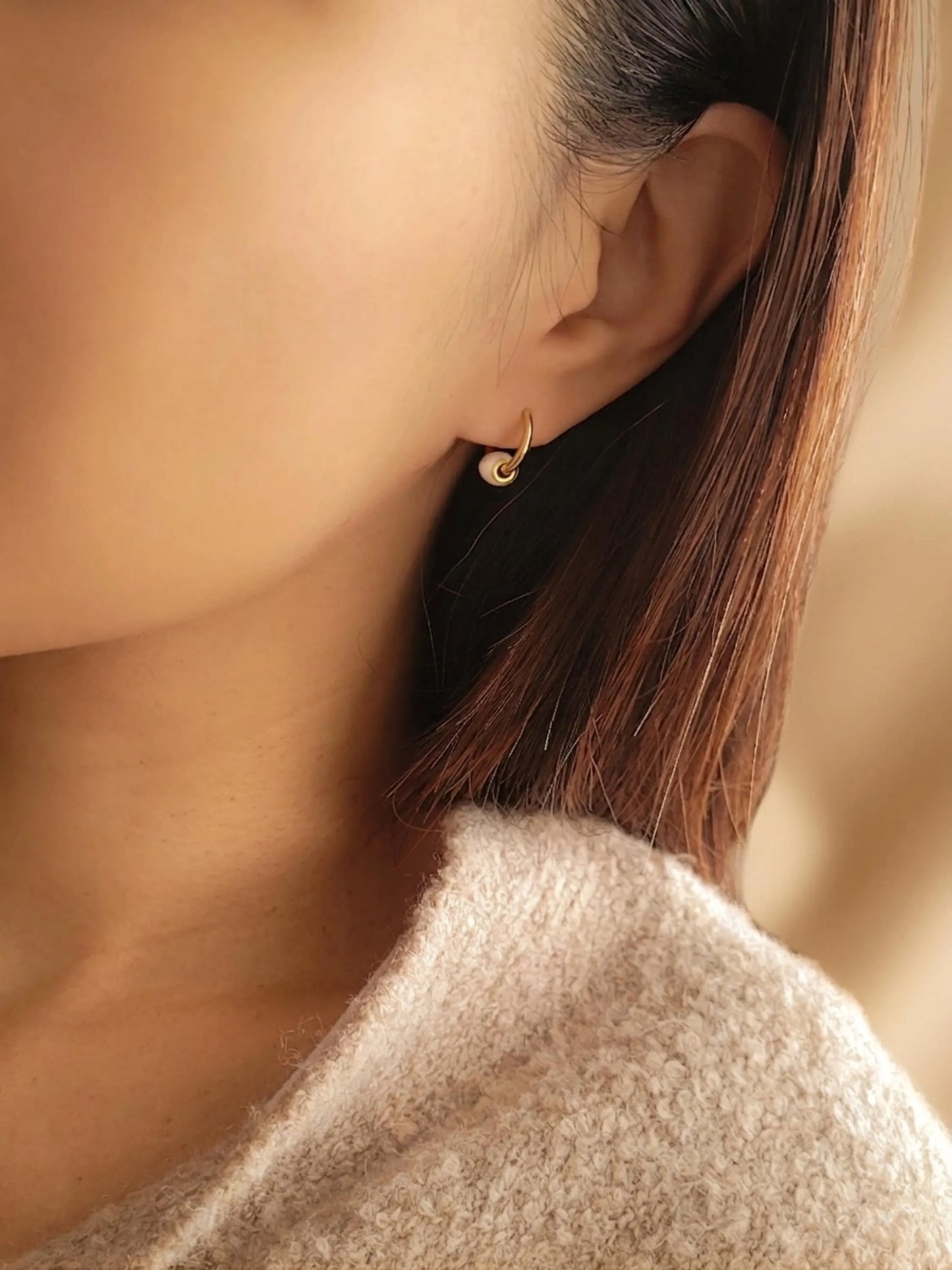 A woman wearing a gold hoop earring with a small white bead charm, minimalist and dainty style.