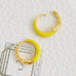 Gold hoop earrings with yellow enamel and gold accents on a textured white surface