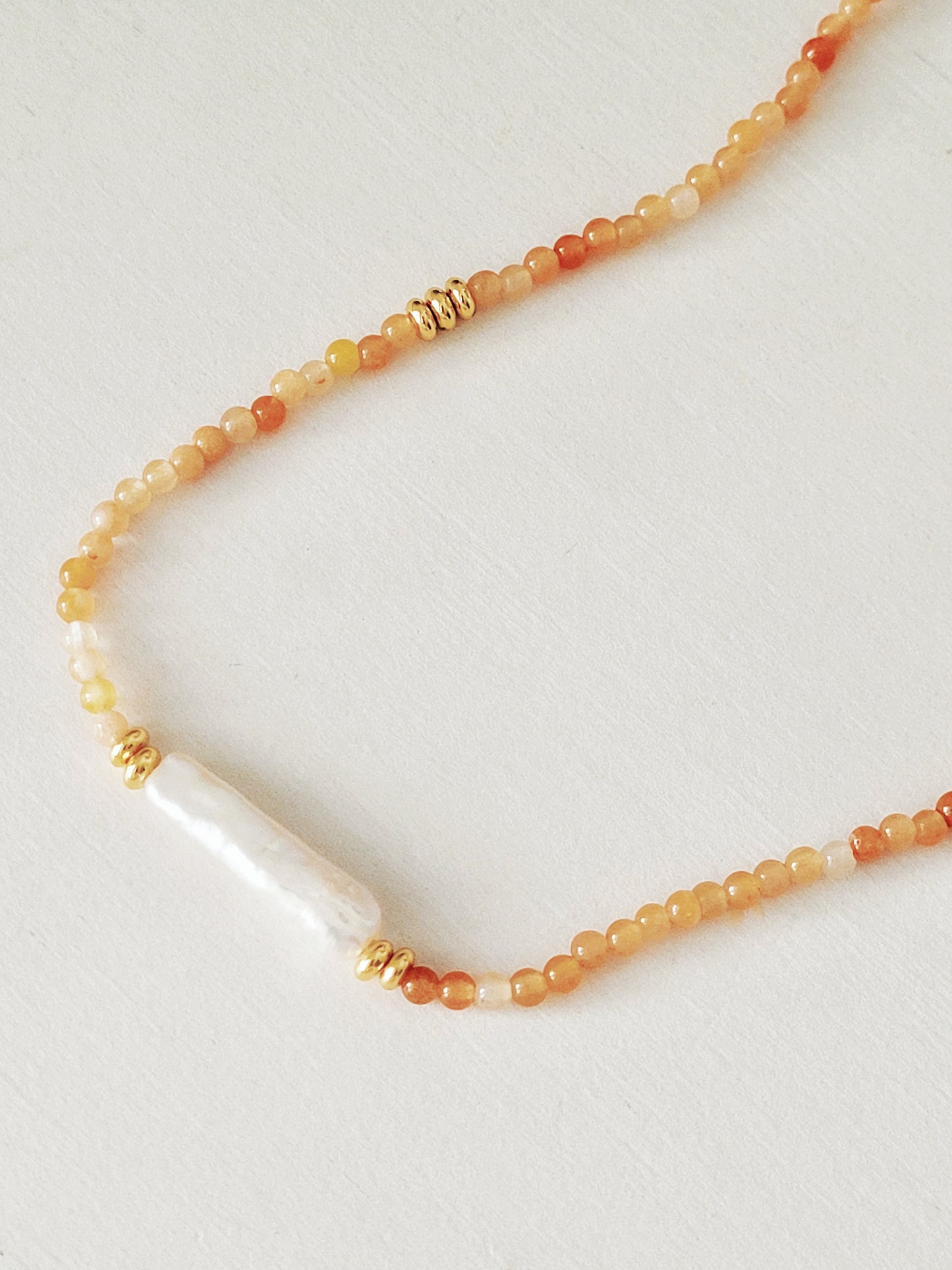 Luxury agate gemstone and freshwater baroque pearl necklace featuring a mix of orange and cream-colored gemstones with gold plated accents.