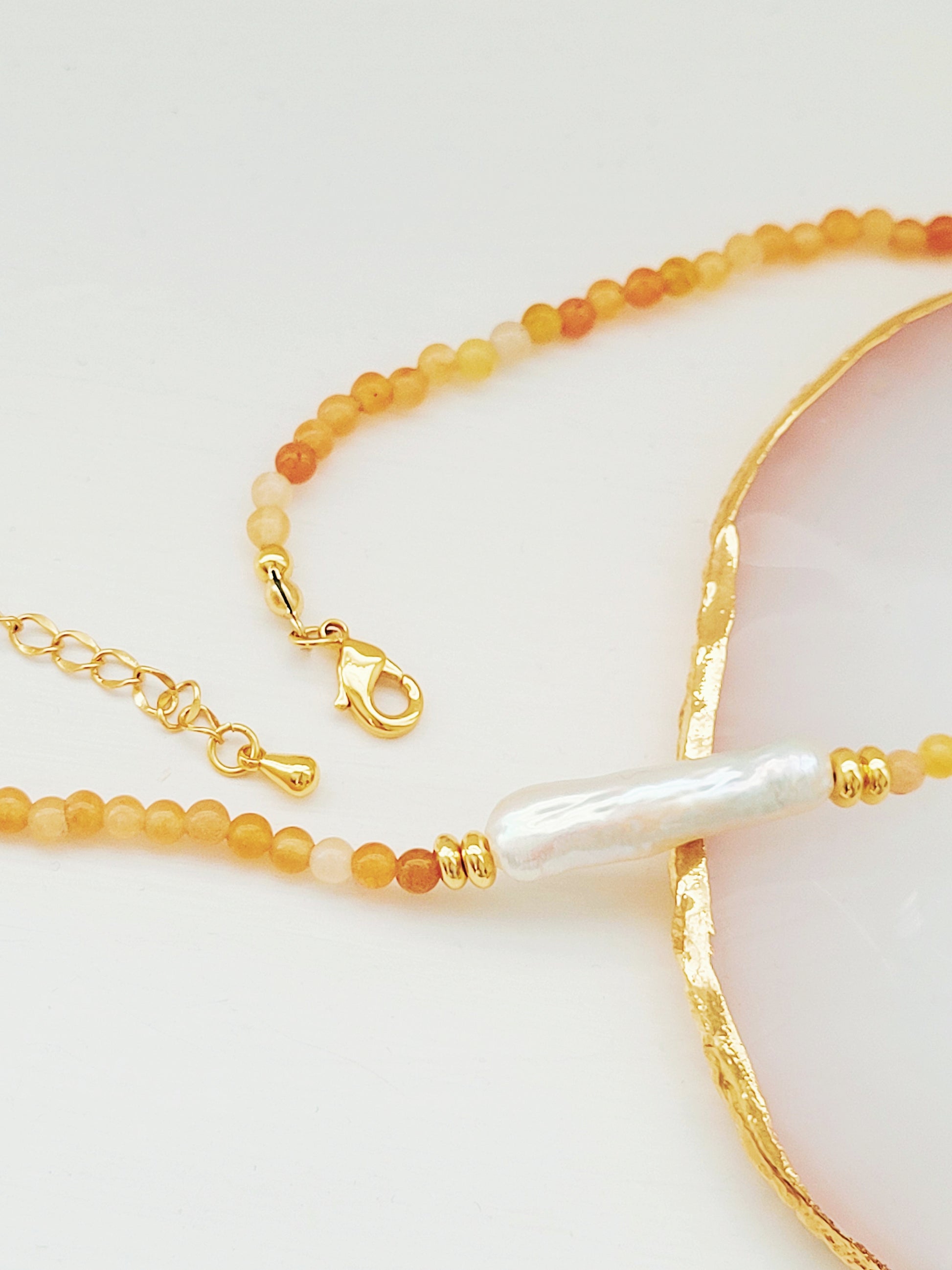 Luxury agate gemstone and freshwater baroque pearl necklace featuring a mix of orange and cream-colored gemstones with gold plated accents.