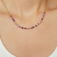 A close-up of a woman wearing a dainty amethyst beaded necklace with faceted purple stones, accented by small gold beads. The necklace with a simple gold chain extending from both sides having purple hues creating a subtle yet stylish look.