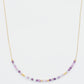A delicate amethyst beaded necklace featuring small faceted amethyst stones in varying shades of purple, interspersed with gold accents. The beads are arranged in a gradient, transitioning from light to deep purple.