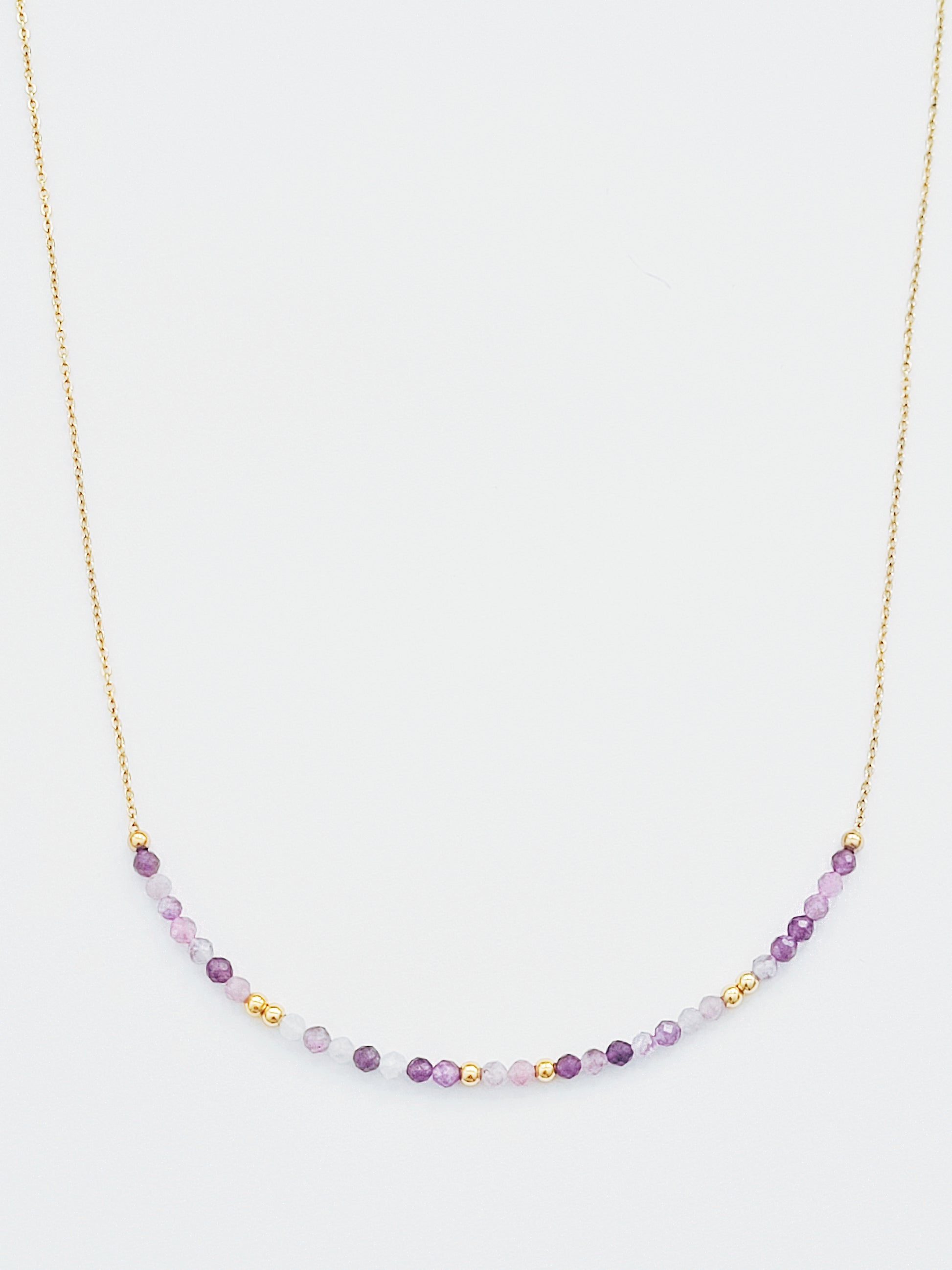 A delicate amethyst beaded necklace featuring small faceted amethyst stones in varying shades of purple, interspersed with gold accents. The beads are arranged in a gradient, transitioning from light to deep purple.